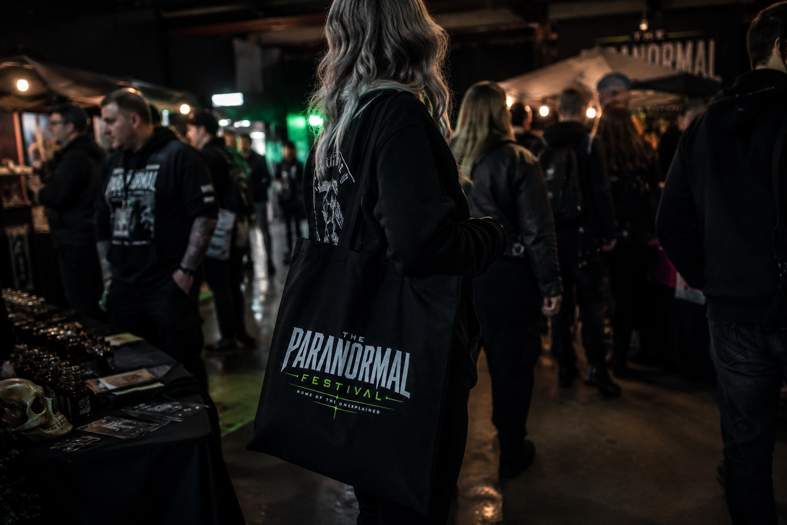 A festival-goer carries a Paranormal Festival tote bag through the candlelit marketplace